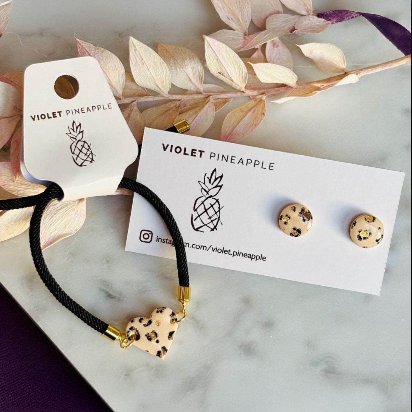 Handcrafted leopard print bracelet and stud earring set with neutral tones and gold accents. Stud earrings are 10mm x 10mm. Set includes an adjustable black corded bracelet. Packaged in a branded gift box.