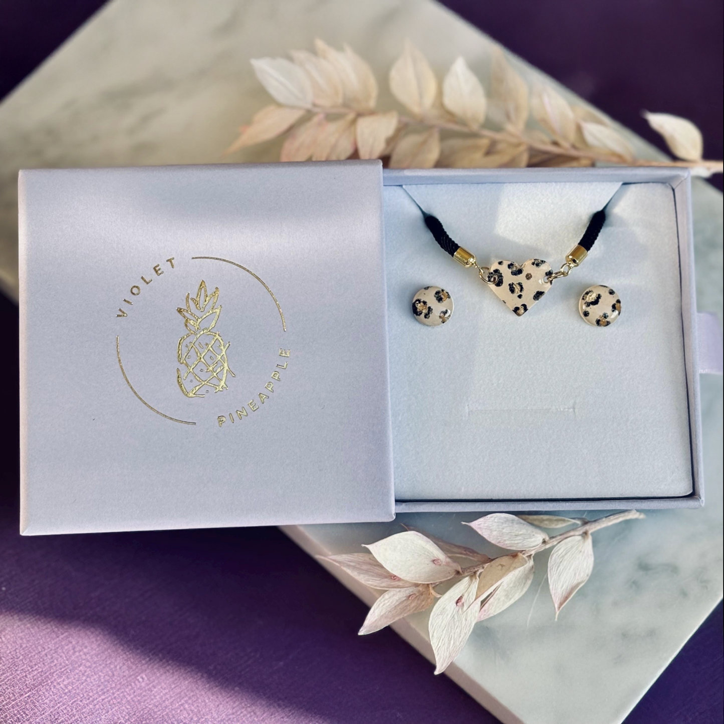 Handcrafted leopard print bracelet and stud earring set with neutral tones and gold accents. Stud earrings are 10mm x 10mm. Set includes an adjustable black corded bracelet. Packaged in a branded gift box