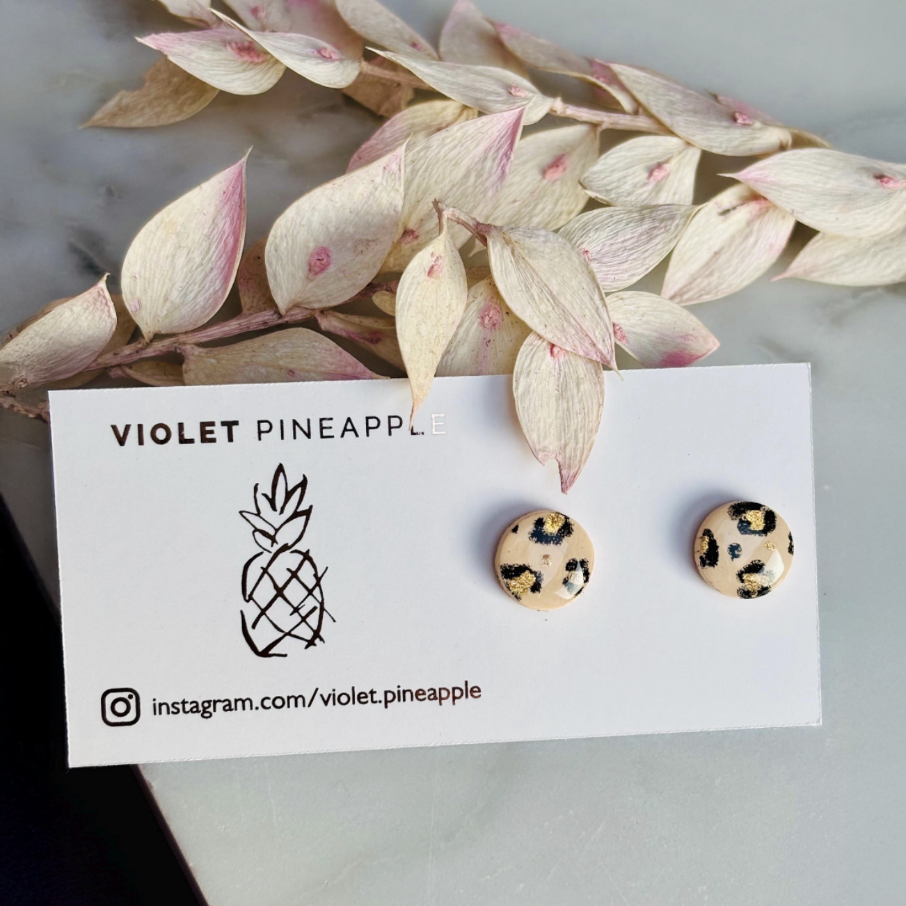 Handcrafted leopard print bracelet and stud earring set with neutral tones and gold accents. Stud earrings are 10mm x 10mm. Set includes an adjustable black corded bracelet. Packaged in a branded gift box