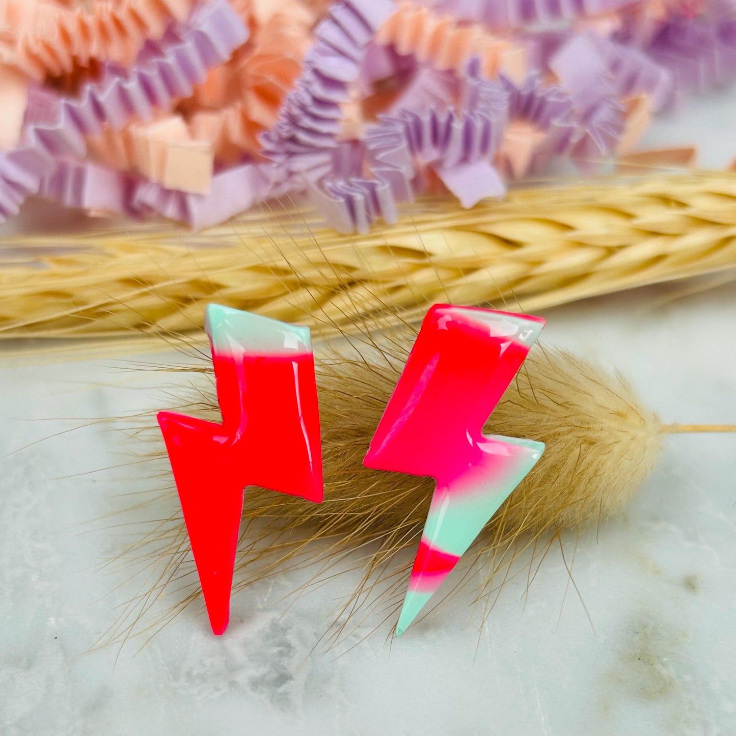 Vibrant 80s-inspired lightning bolt stud earrings, handmade with polymer clay. Features a neon pink and mint ombré design.