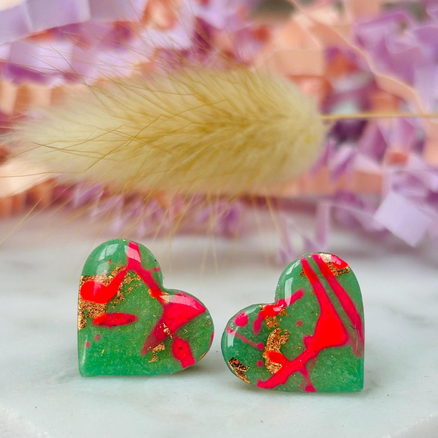 Vibrant neon pink heart-shaped stud earrings, handmade with polymer clay. Features an abstract design with gold foil accents.