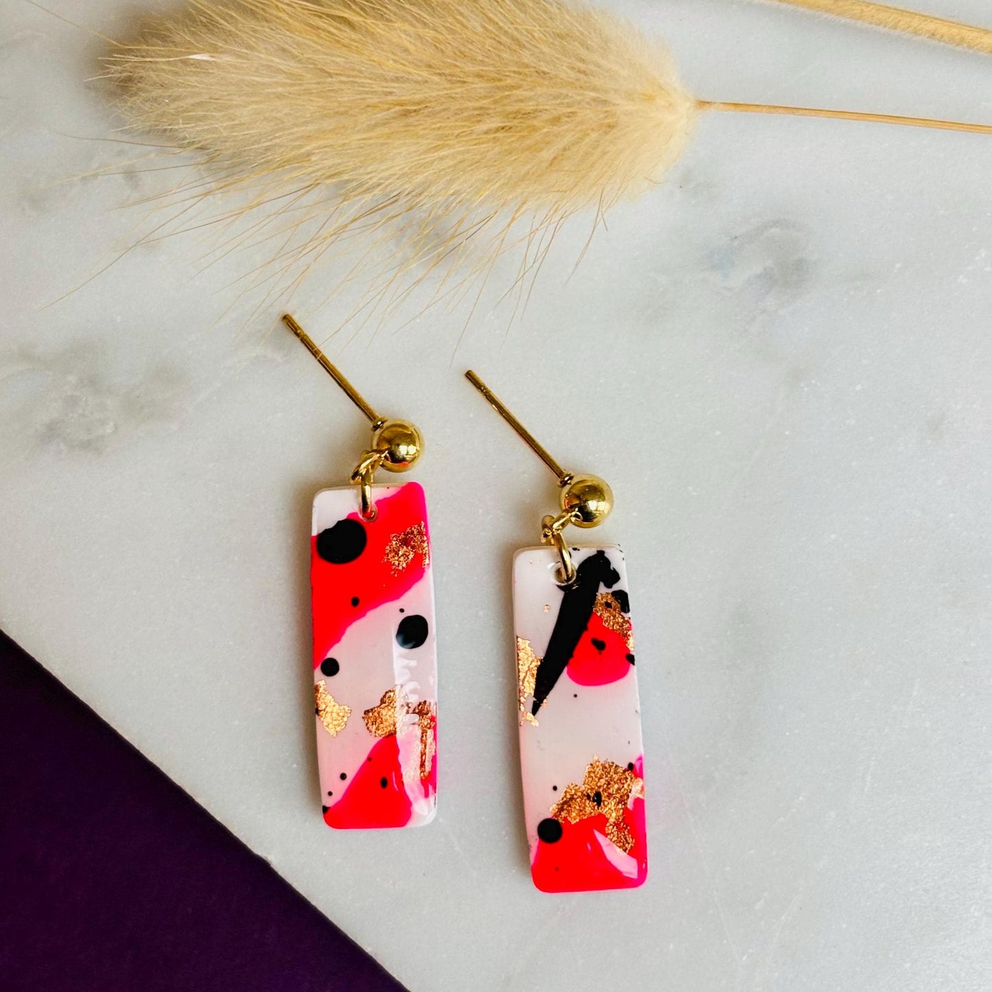 Edgy drop stud earrings with a unique design featuring white, neon pink, rose gold foil, and black ink, handmade with polymer clay.