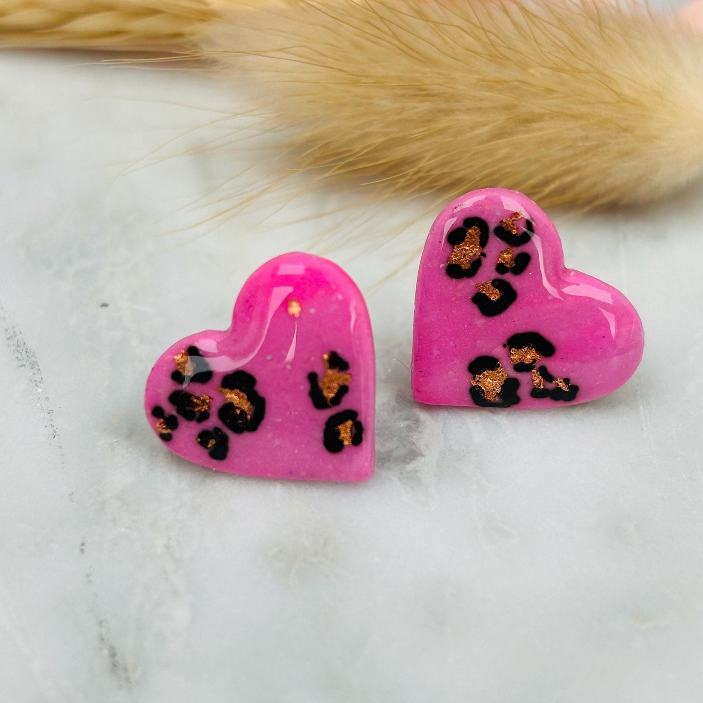 Chic pink heart-shaped stud earrings with a handpainted leopard print, handmade with polymer clay.