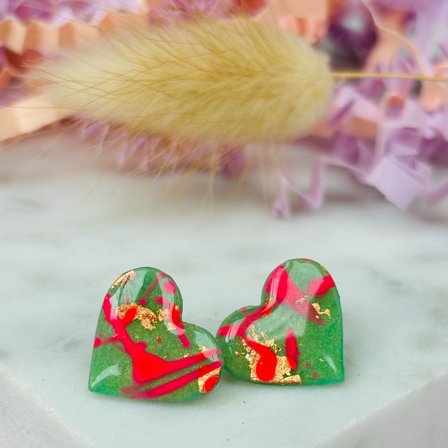 Vibrant neon pink heart-shaped stud earrings, handmade with polymer clay. Features an abstract design with gold foil accents.