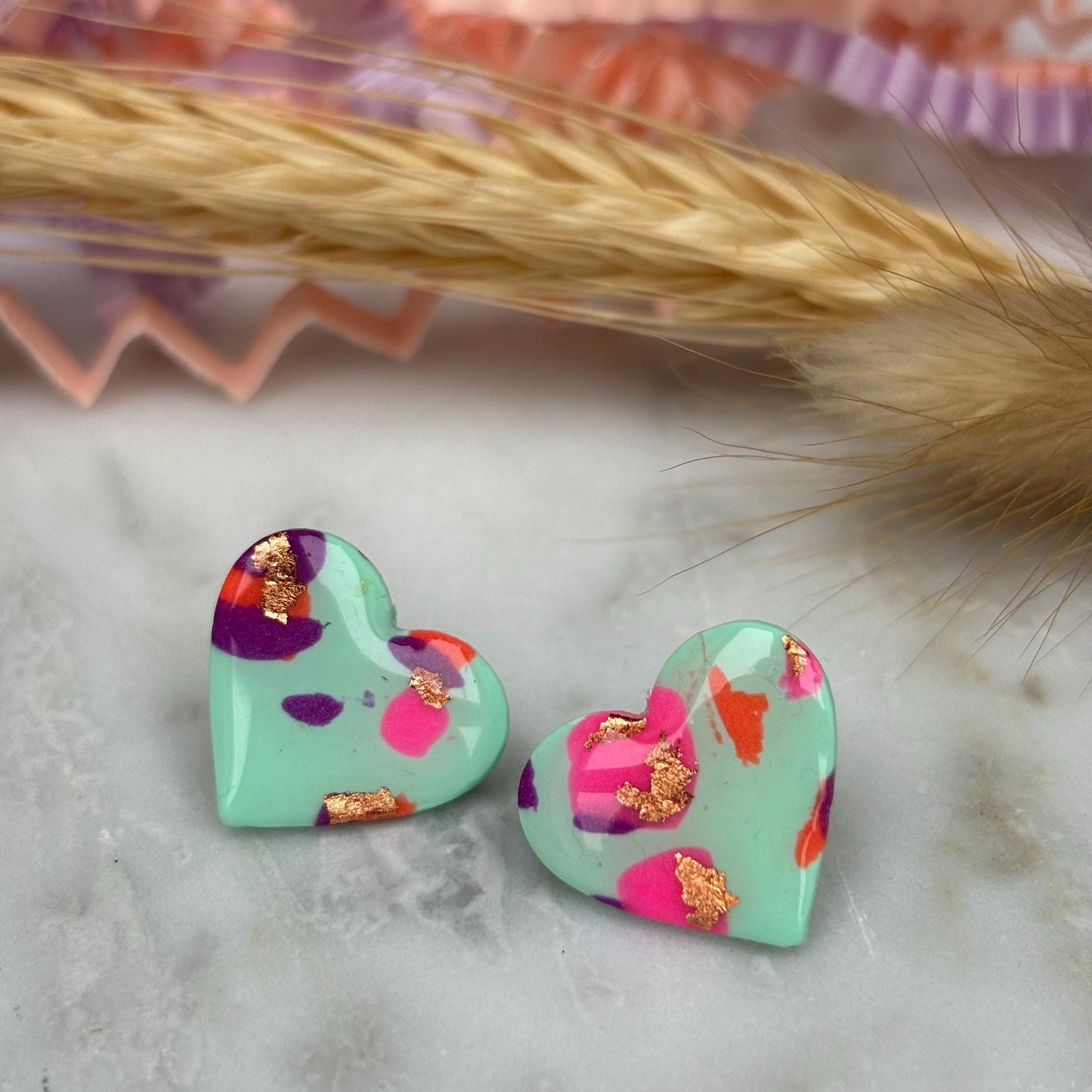Vibrant 90s-inspired heart-shaped stud earrings, handmade with polymer clay. Features a blend of mint green, pink, orange, and gold leaf accents.