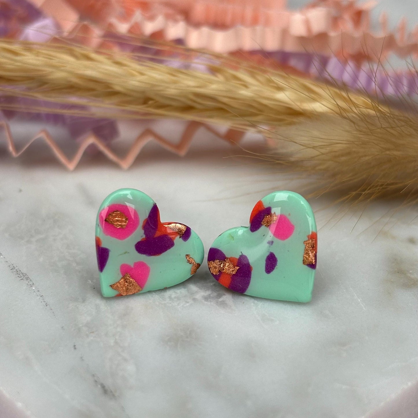 Vibrant 90s-inspired heart-shaped stud earrings, handmade with polymer clay. Features a blend of mint green, pink, orange, and gold leaf accents.
