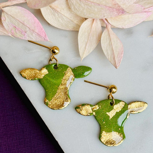 Cute cow drop stud earrings with olive green and gold foil details, handmade with polymer clay.