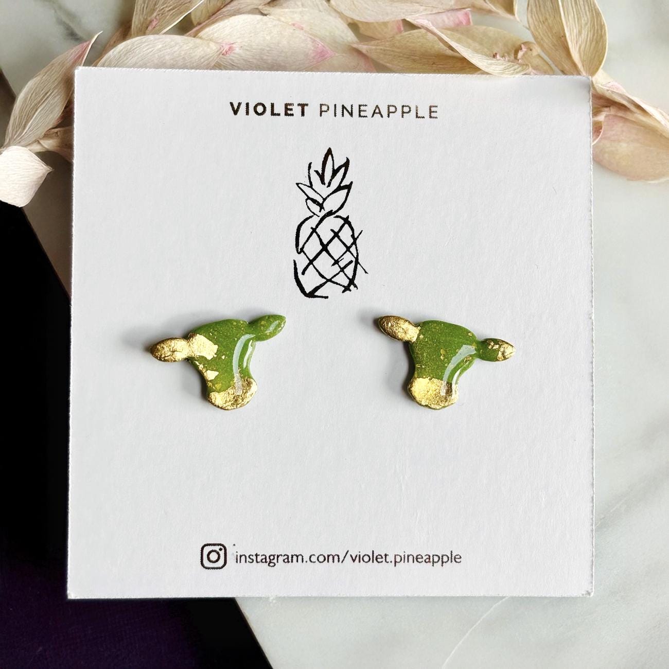 Close-up of small green cow stud earrings with gold foil.