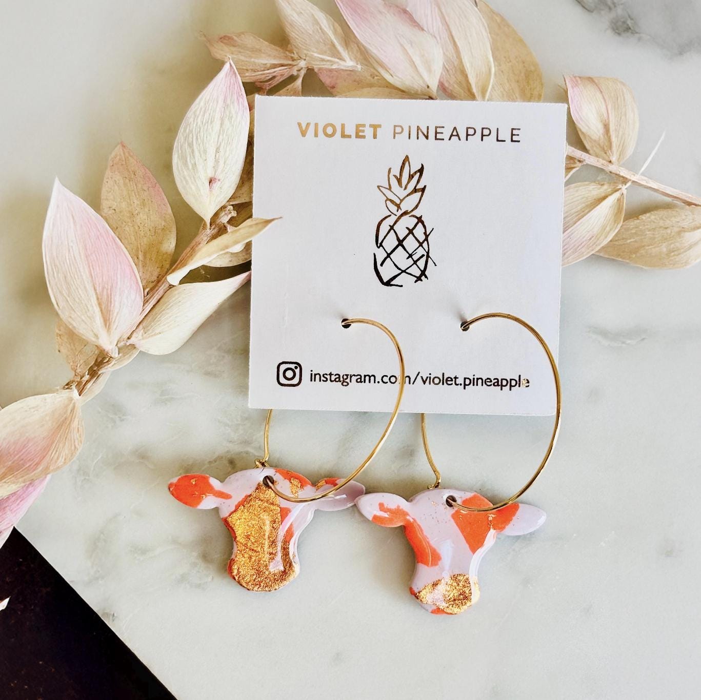 Close-up of vibrant orange cow hoop earring with rose gold foil detail.