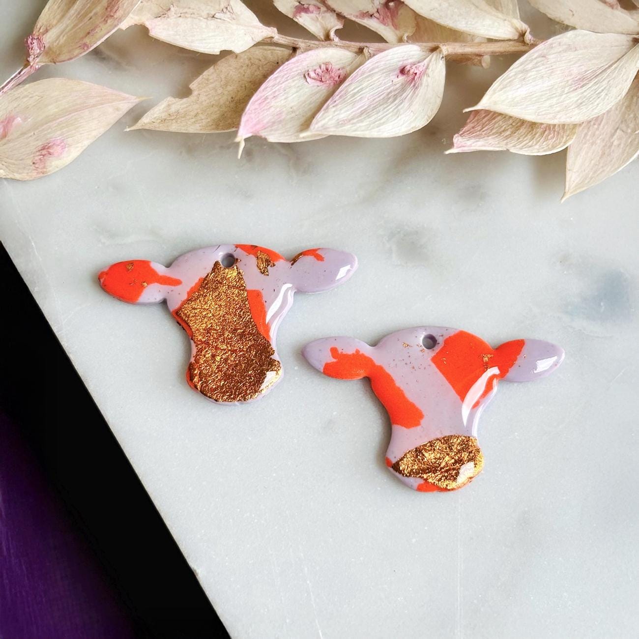 Close-up of vibrant orange cow hoop earring with rose gold foil detail.