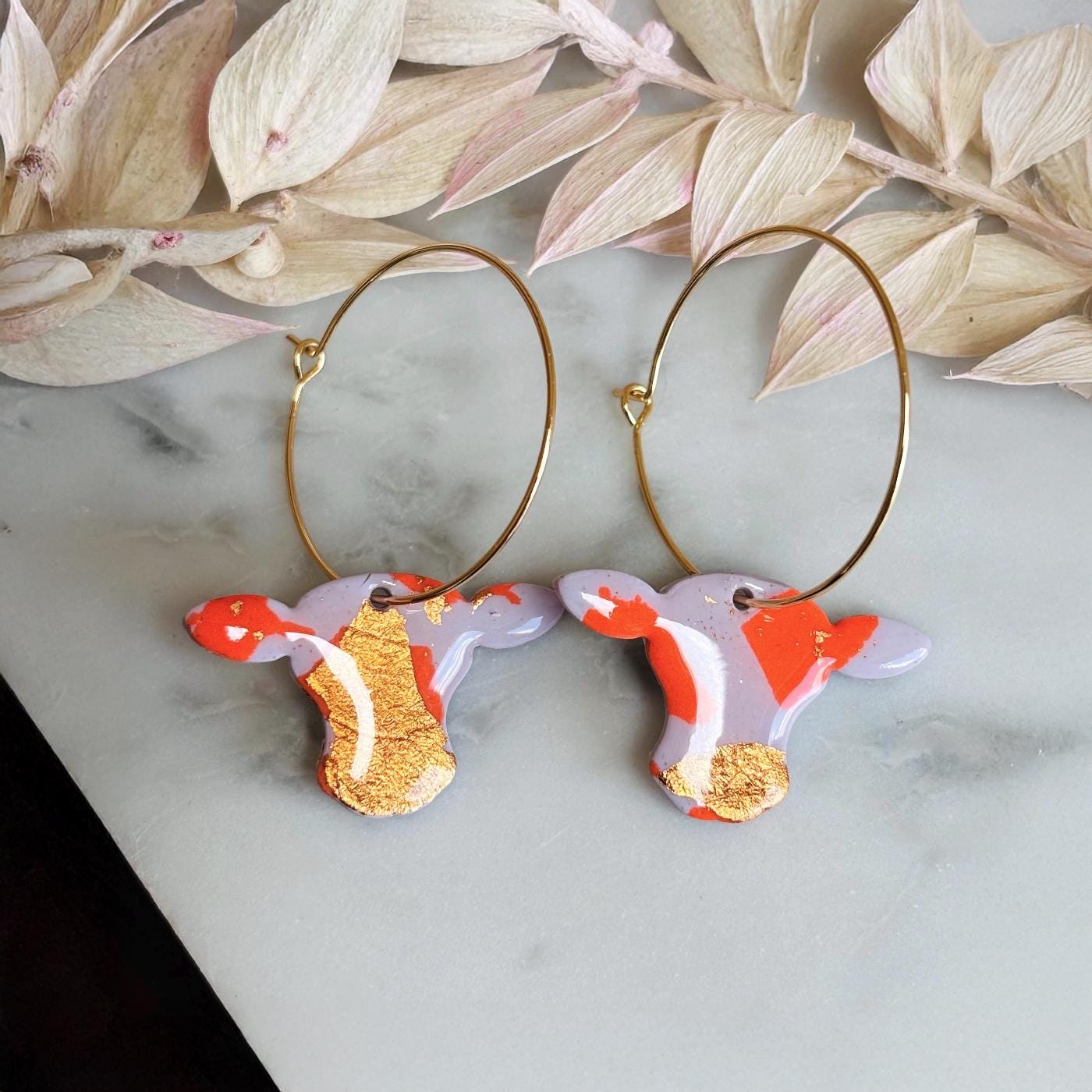 Close-up of vibrant orange cow hoop earring with rose gold foil detail.