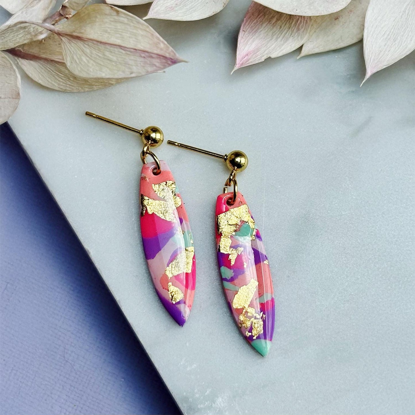 Colourful surfboard-shaped surf earrings with gold foil details, handmade from polymer clay, featuring hypoallergenic surgical stainless steel posts and backings.