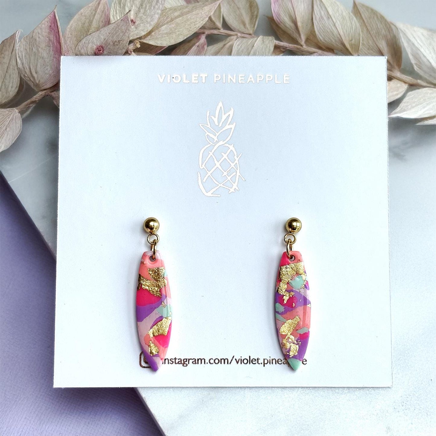 Colourful surfboard-shaped surf earrings with gold foil details, handmade from polymer clay, featuring hypoallergenic surgical stainless steel posts and backings.
