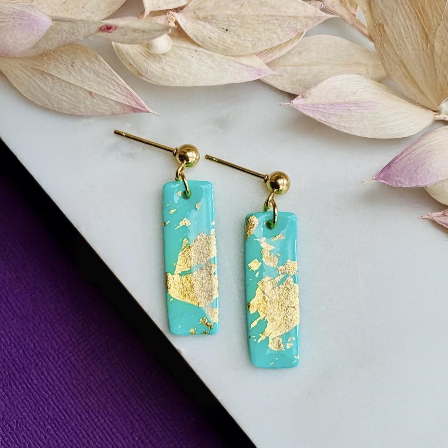 Bold, handmade teal polymer clay drop earrings with elegant gold foil detailing, shown from a close-up angle.