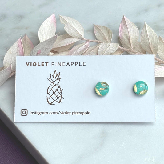 Mini teal and gold polymer clay stud earrings, with a focus on their textured surface and reflective gold details