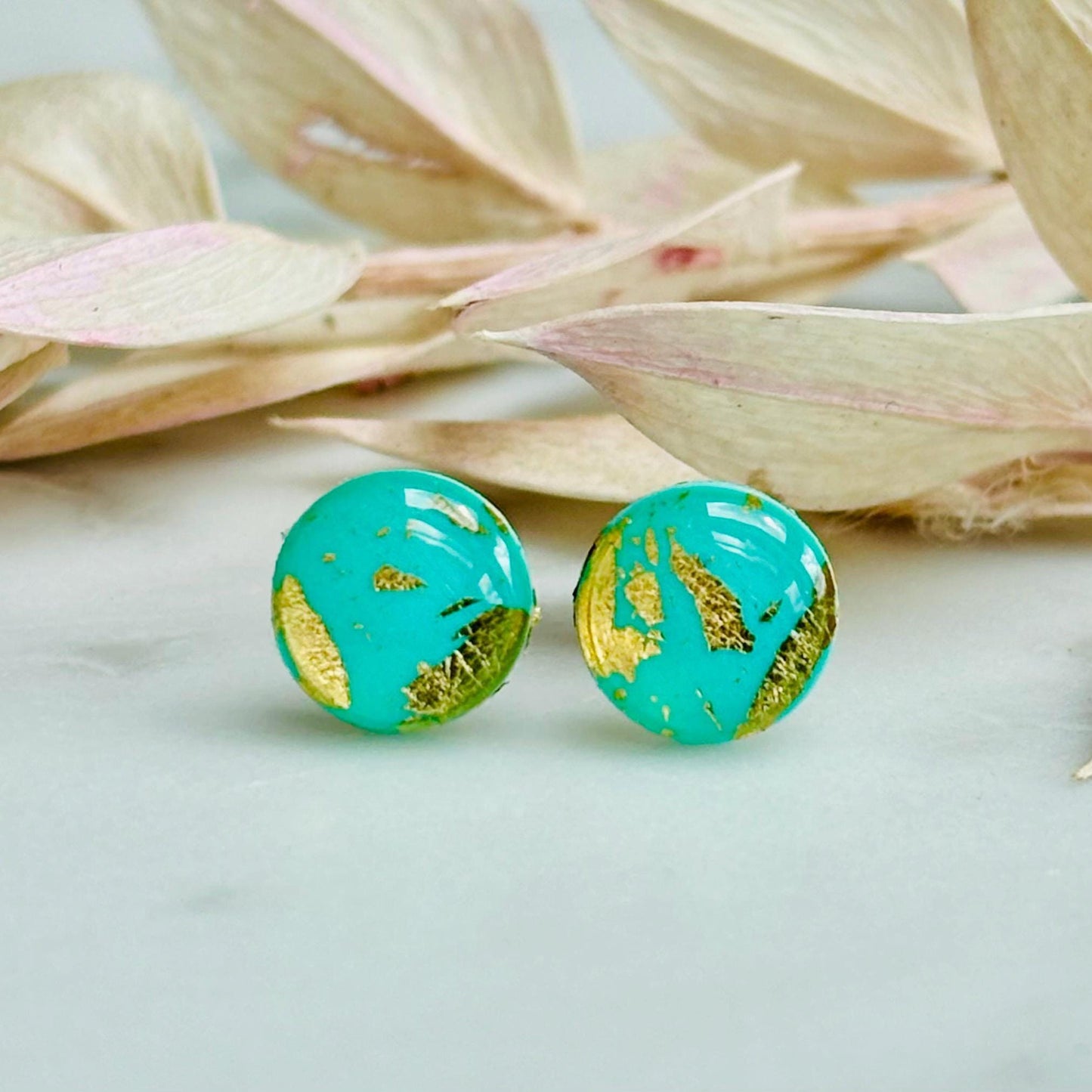 Mini teal and gold polymer clay stud earrings, with a focus on their textured surface and reflective gold details