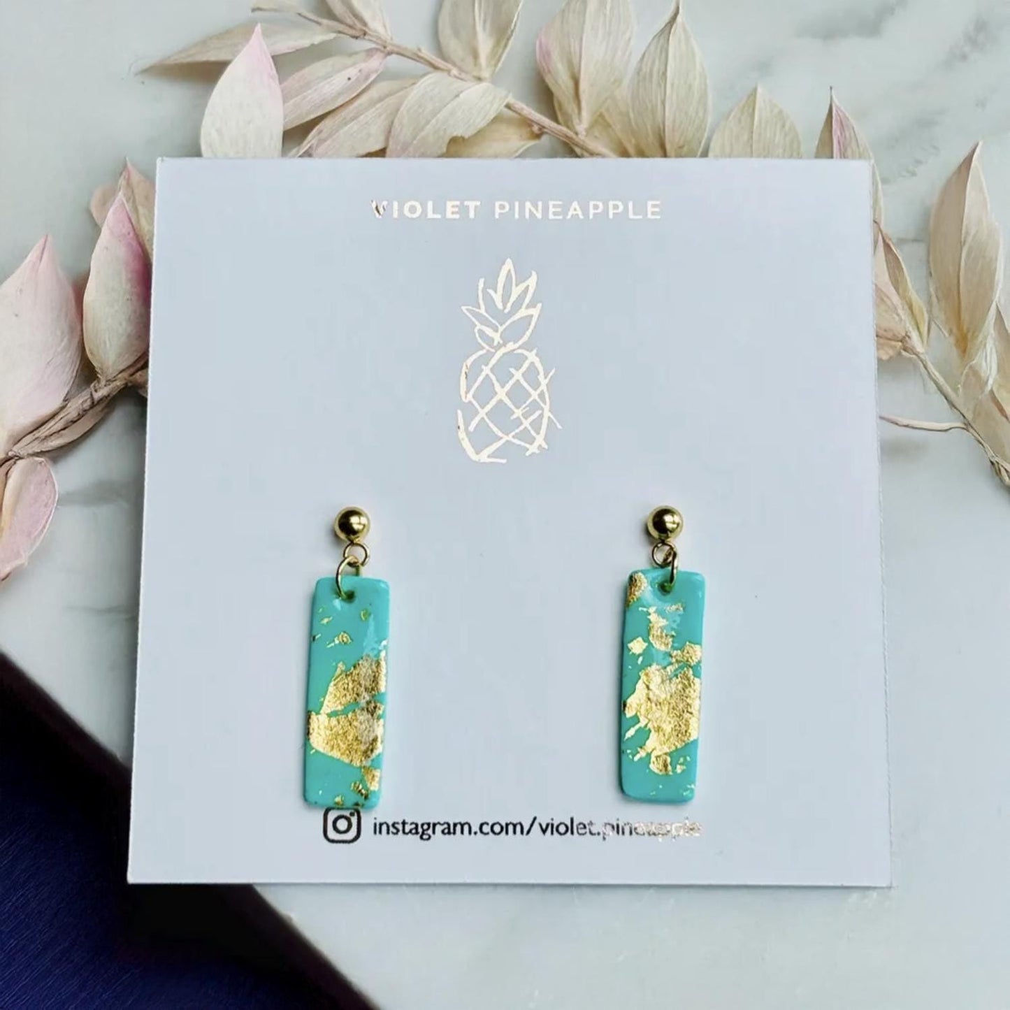 Turquoise earrings with gold accents on a 'Violet Pineapple' branded card.