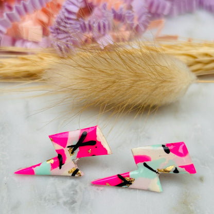 Vibrant 90s-inspired lightning bolt stud earrings, handmade with polymer clay. Features magenta, mint, gold, and ebony ink accents.
