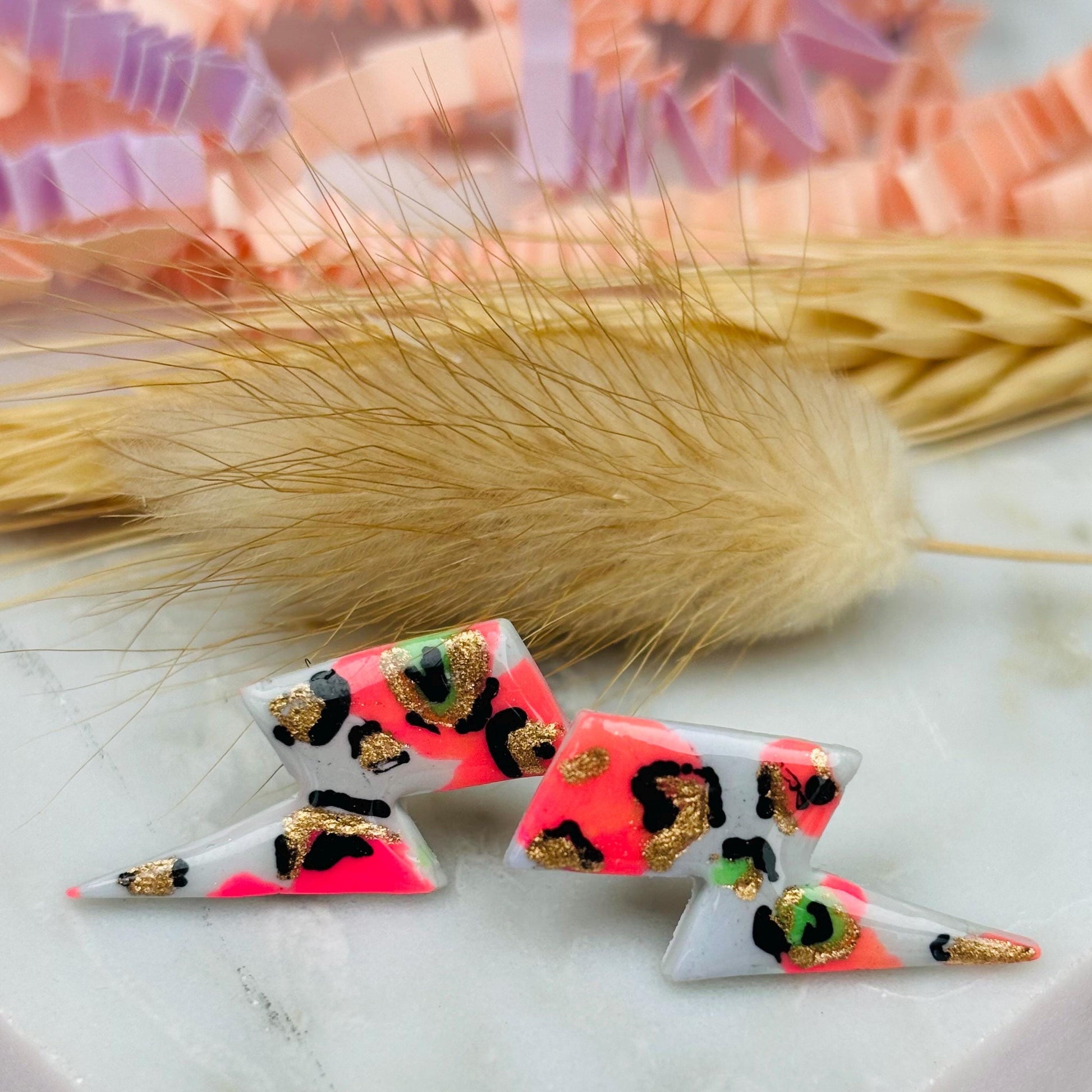 Vibrant leopard print lightning bolt stud earrings, handmade with polymer clay. Features a playful mix of peachy pink and bright green.