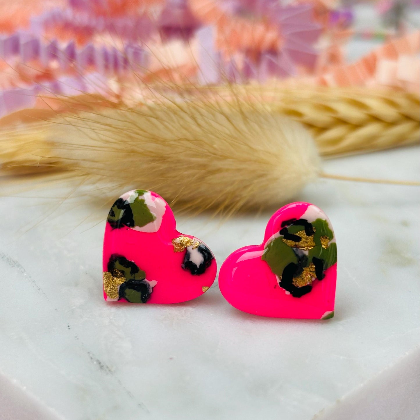 Vibrant neon pink heart-shaped stud earrings with a handpainted leopard print, handmade with polymer clay