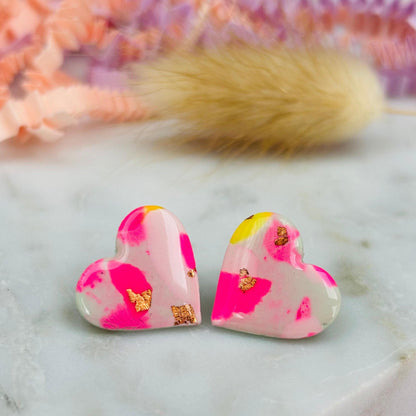 Delicate pastel-coloured heart-shaped stud earrings, handmade with polymer clay. Features soft pink, and yellow with gold leaf accents.