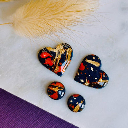Abstract heart-shaped stud earrings with navy blue, vibrant orange, and gold splatter details, handmade with polymer clay.