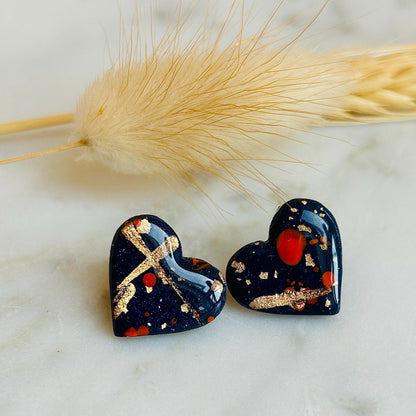 Abstract heart-shaped stud earrings with navy blue, vibrant orange, and gold splatter details, handmade with polymer clay.