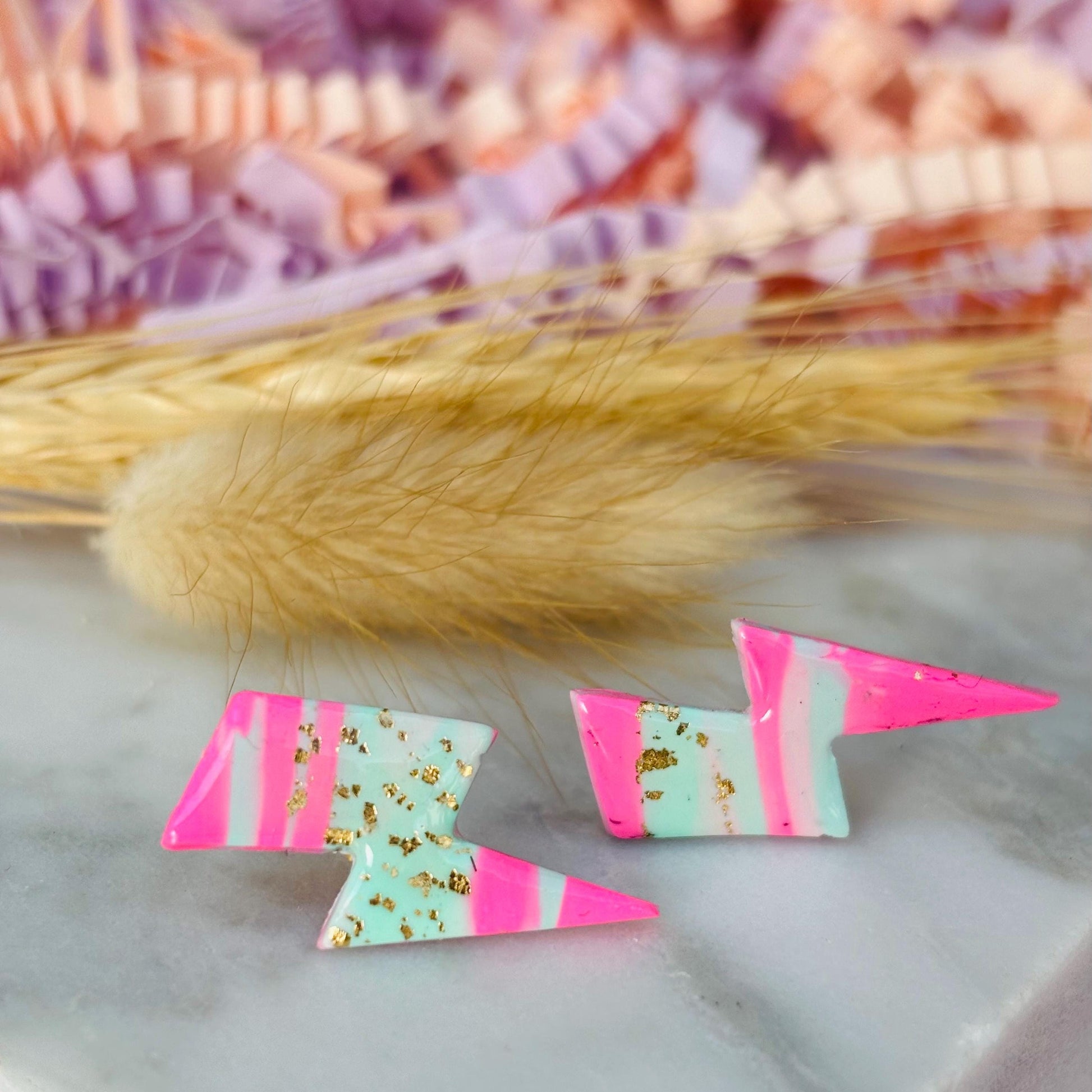 Vibrant 80s ski-inspired lightning bolt stud earrings, handmade with polymer clay. Features soft pink, mint green, and gold leaf accents.