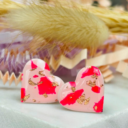 Vibrant pink heart-shaped stud earrings, handmade with polymer clay. Features rose gold leaf accents.