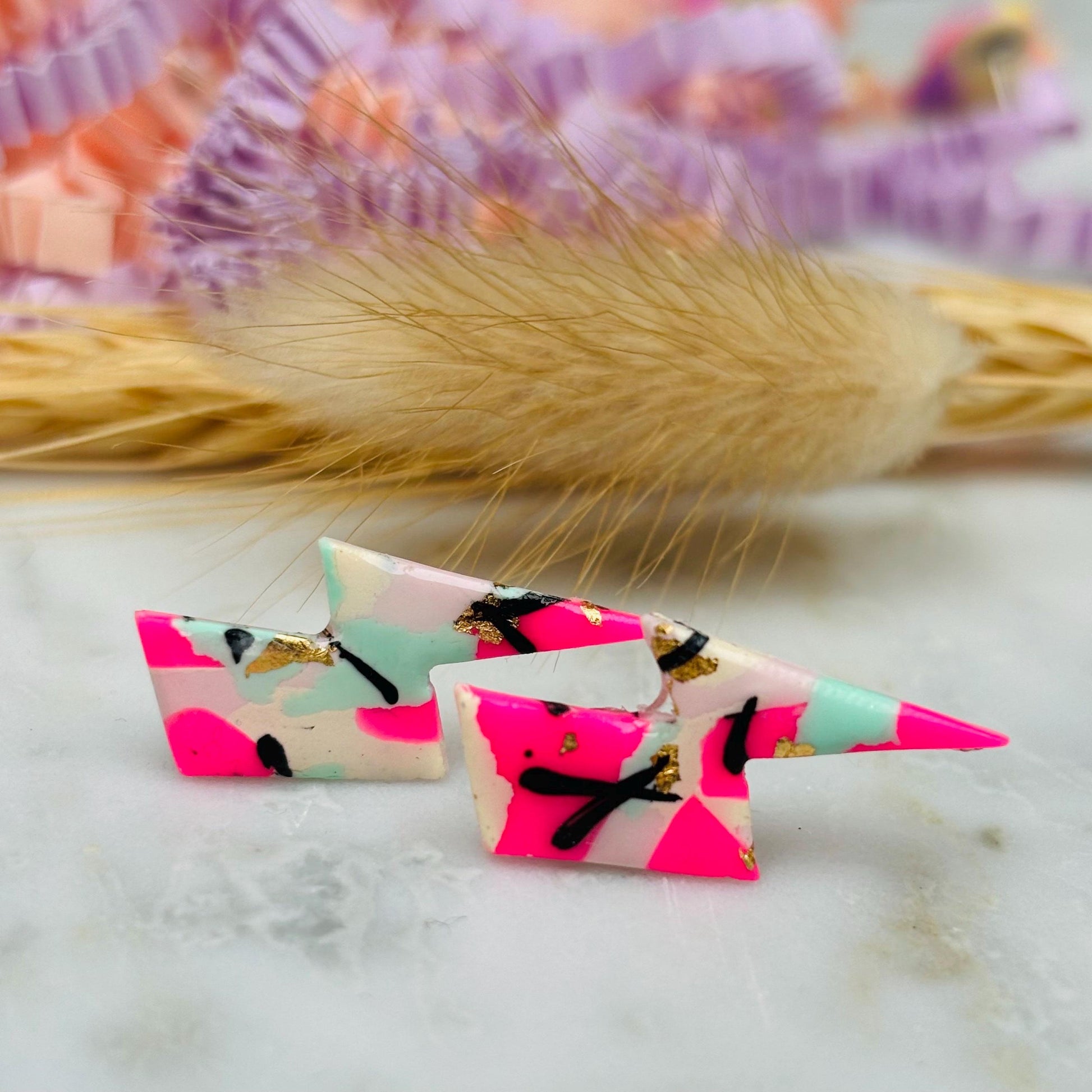 Vibrant 90s-inspired lightning bolt stud earrings, handmade with polymer clay. Features magenta, mint, gold, and ebony ink accents.