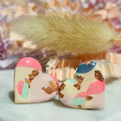 Soft pink heart-shaped stud earrings with rose gold accents, handmade with polymer clay.