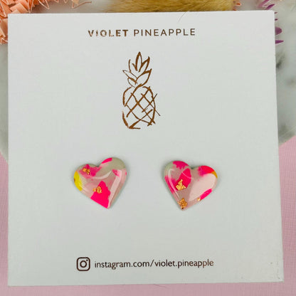 Delicate pastel-coloured heart-shaped stud earrings, handmade with polymer clay. Features soft pink, and yellow with gold leaf accents.