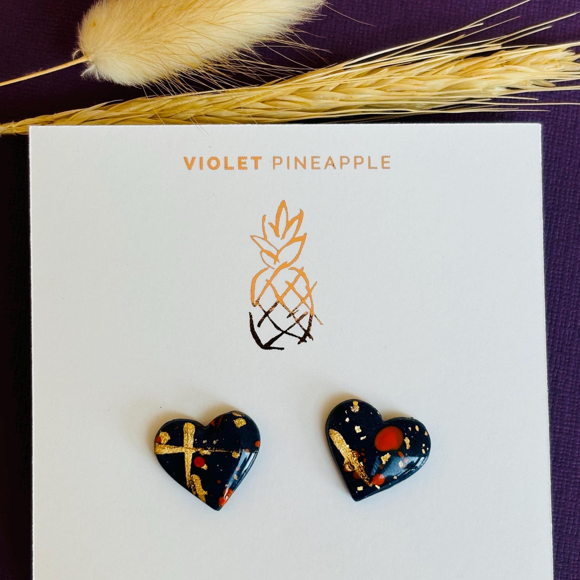 Abstract heart-shaped stud earrings with navy blue, vibrant orange, and gold splatter details, handmade with polymer clay.