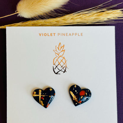 Abstract heart-shaped stud earrings with navy blue, vibrant orange, and gold splatter details, handmade with polymer clay.