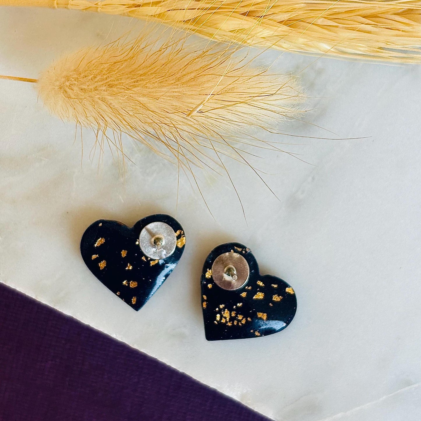 Abstract heart-shaped stud earrings with navy blue, vibrant orange, and gold splatter details, handmade with polymer clay.