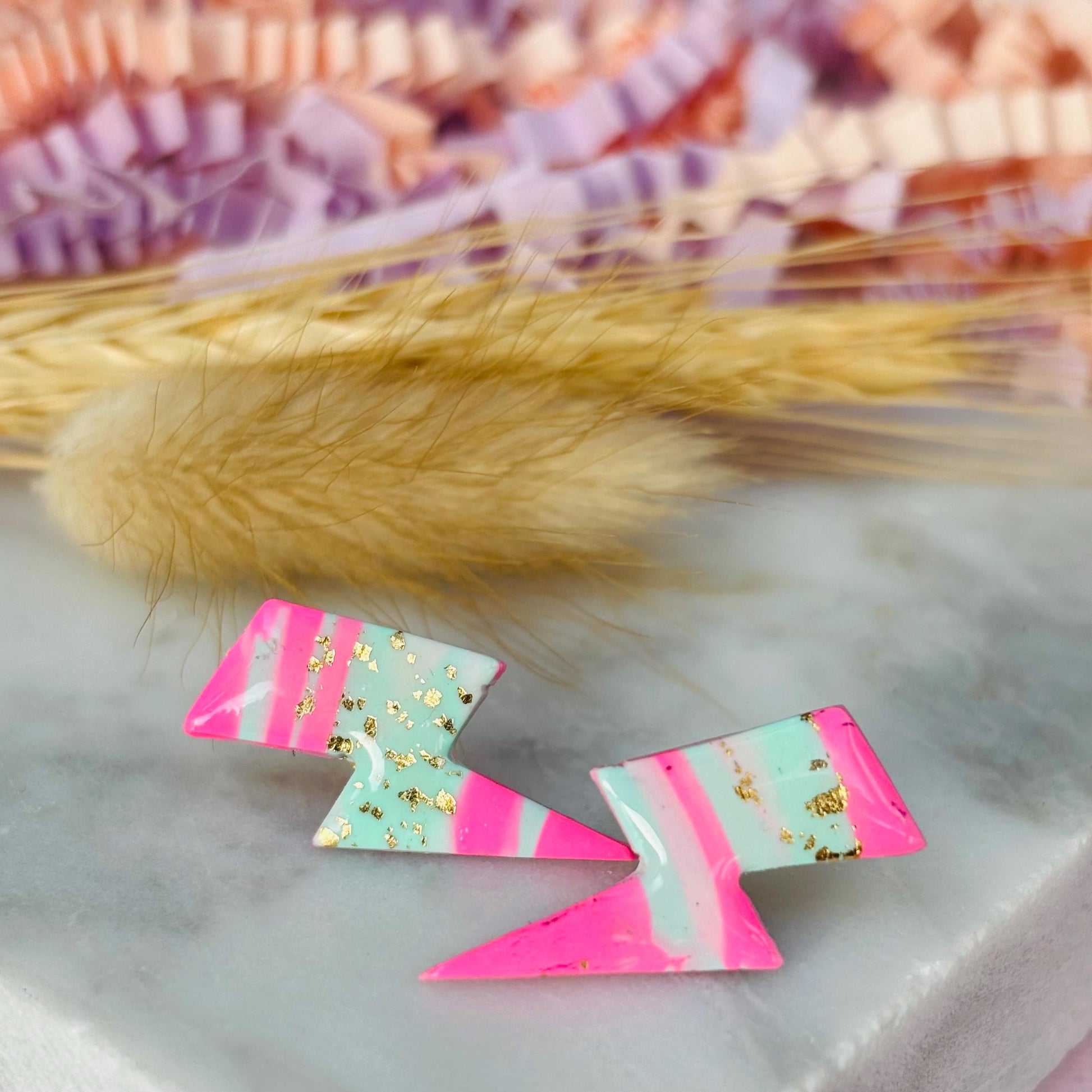 Vibrant 80s ski-inspired lightning bolt stud earrings, handmade with polymer clay. Features soft pink, mint green, and gold leaf accents.