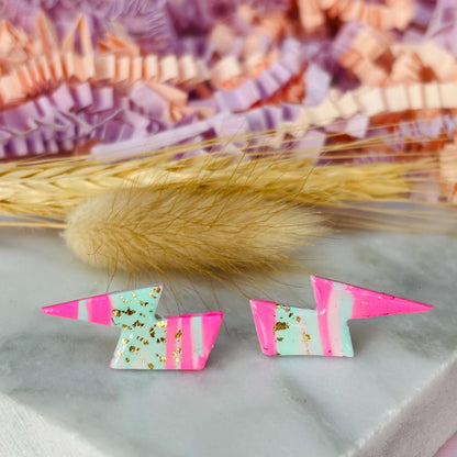 Vibrant 80s ski-inspired lightning bolt stud earrings, handmade with polymer clay. Features soft pink, mint green, and gold leaf accents.