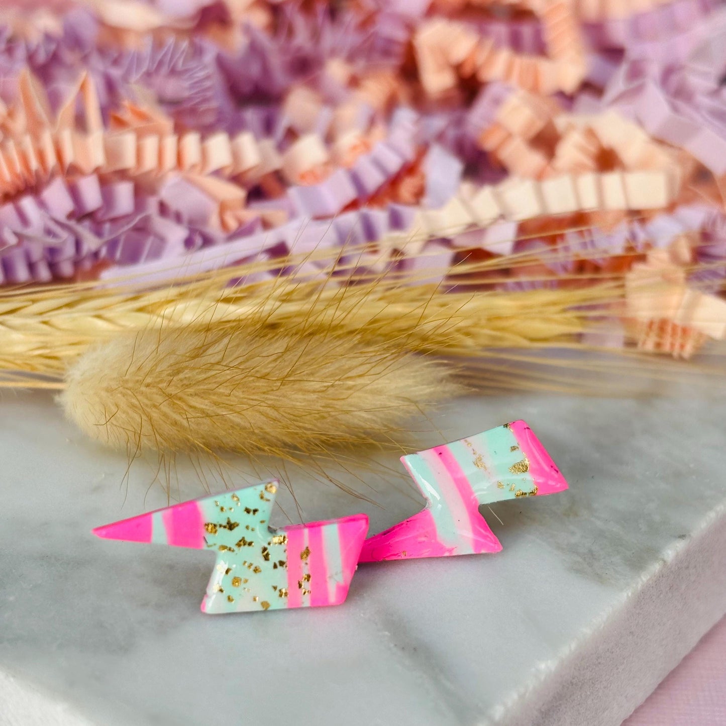 Vibrant 80s ski-inspired lightning bolt stud earrings, handmade with polymer clay. Features soft pink, mint green, and gold leaf accents.