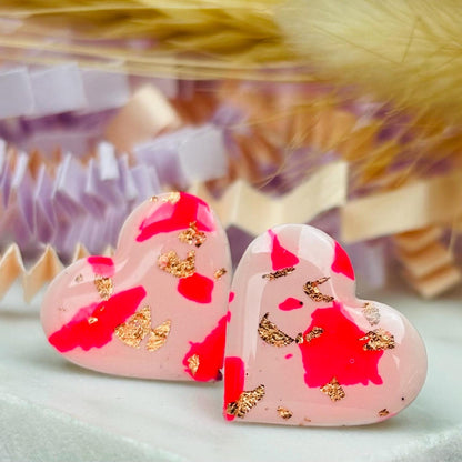 Vibrant pink heart-shaped stud earrings, handmade with polymer clay. Features rose gold leaf accents.