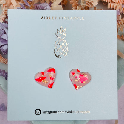 Vibrant pink heart-shaped stud earrings, handmade with polymer clay. Features rose gold leaf accents.