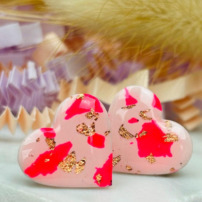 Vibrant pink heart-shaped stud earrings, handmade with polymer clay. Features rose gold leaf accents.