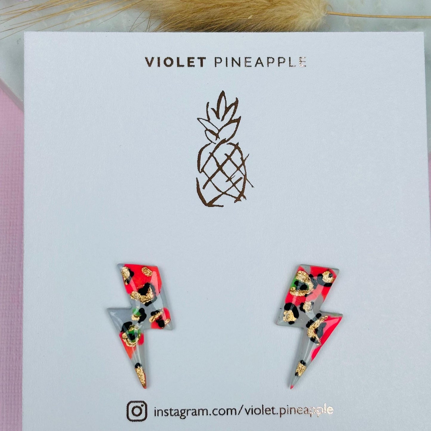 Vibrant leopard print lightning bolt stud earrings, handmade with polymer clay. Features a playful mix of peachy pink and bright green.