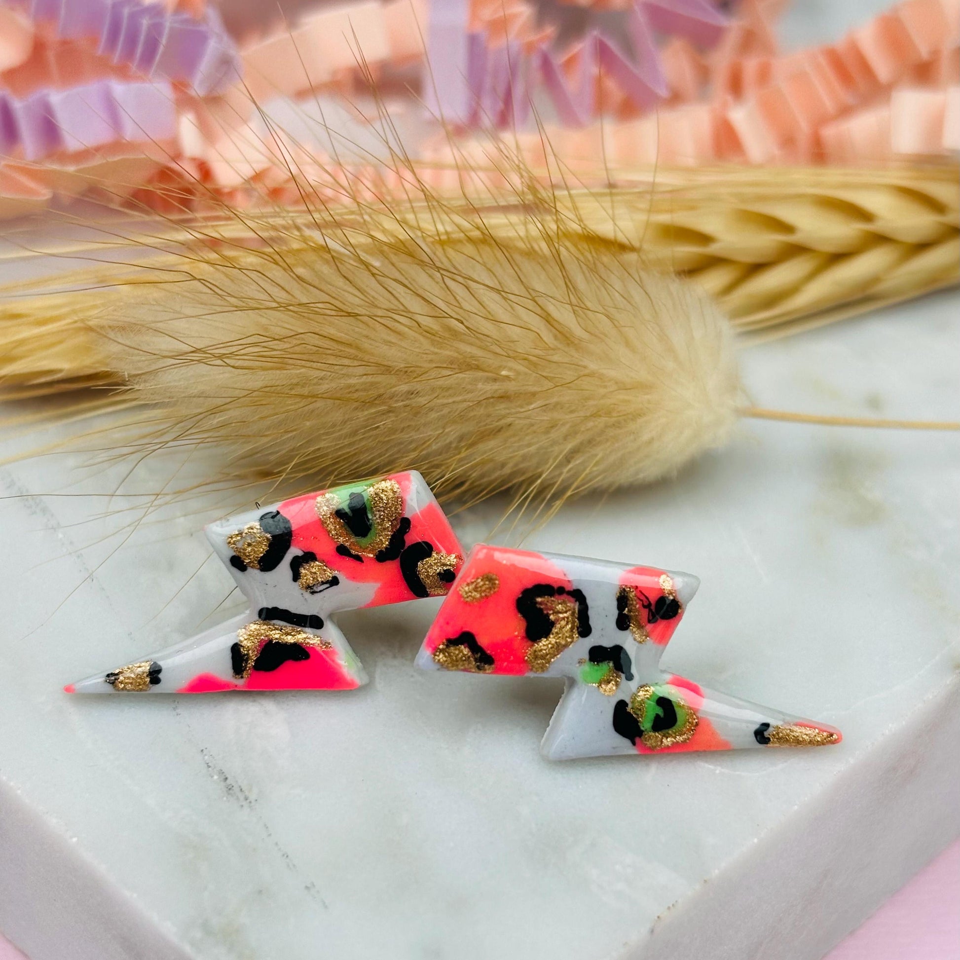 Vibrant leopard print lightning bolt stud earrings, handmade with polymer clay. Features a playful mix of peachy pink and bright green.