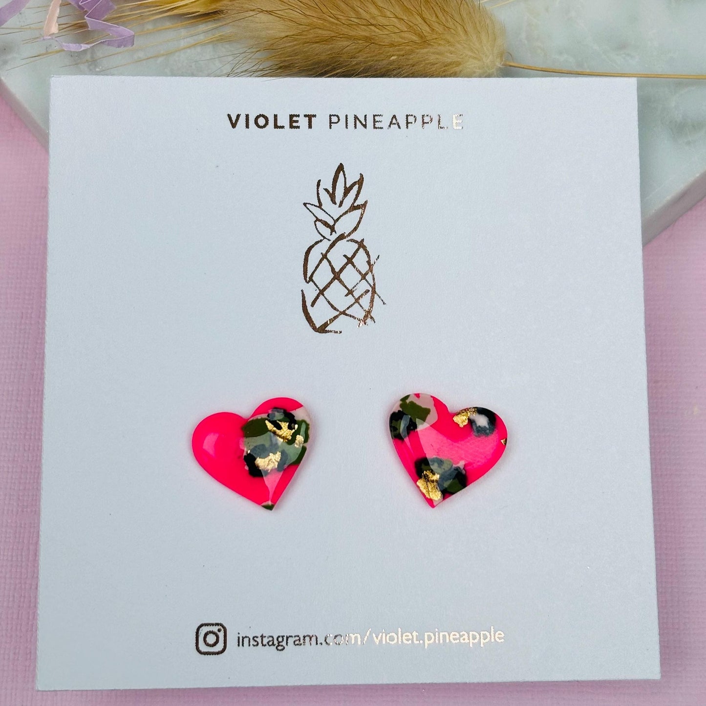Vibrant neon pink heart-shaped stud earrings with a handpainted leopard print, handmade with polymer clay