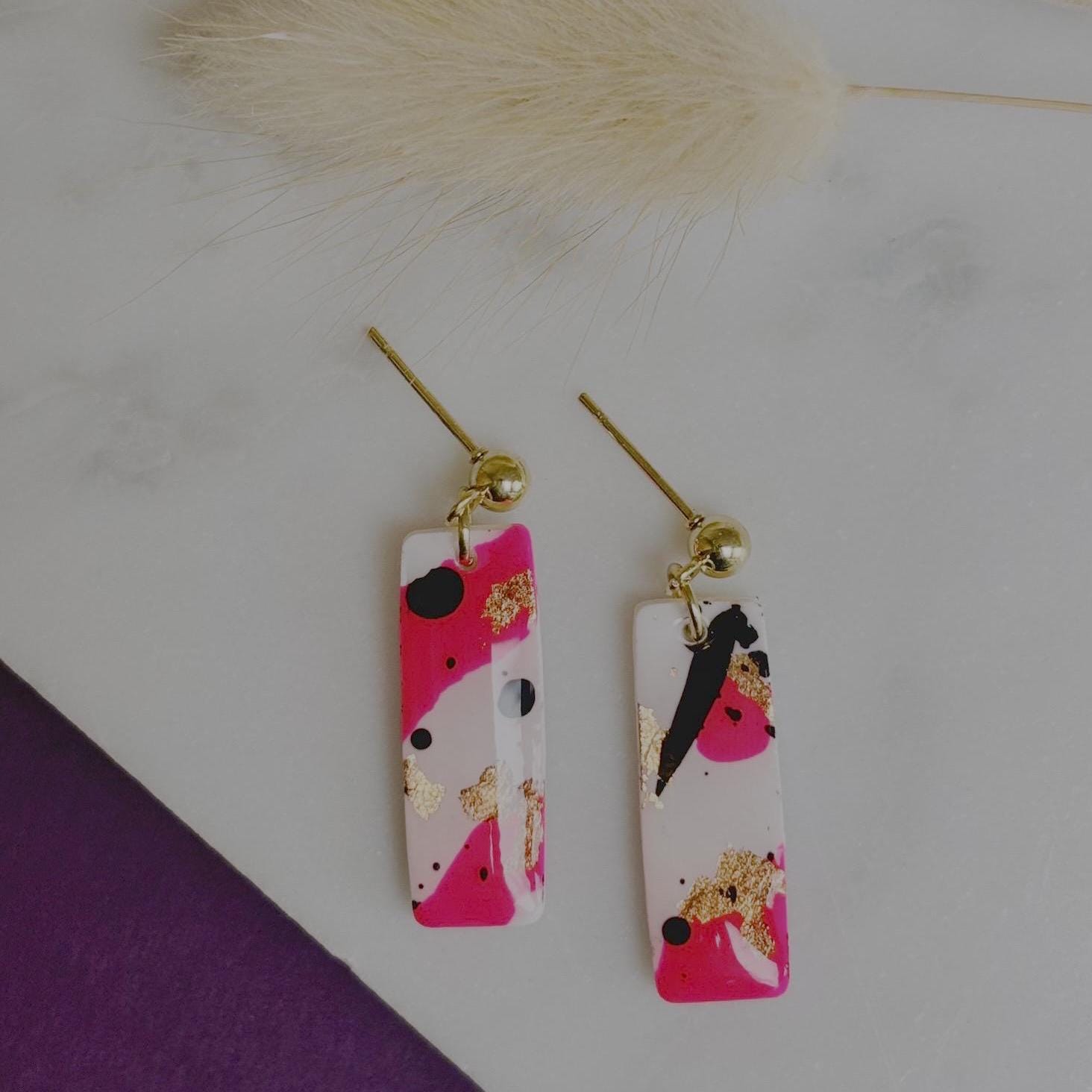 Edgy drop stud earrings with a unique design featuring white, neon pink, rose gold foil, and black ink, handmade with polymer clay.