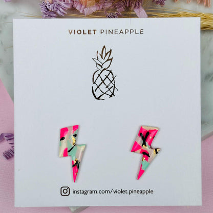 Vibrant 90s-inspired lightning bolt stud earrings, handmade with polymer clay. Features magenta, mint, gold, and ebony ink accents.