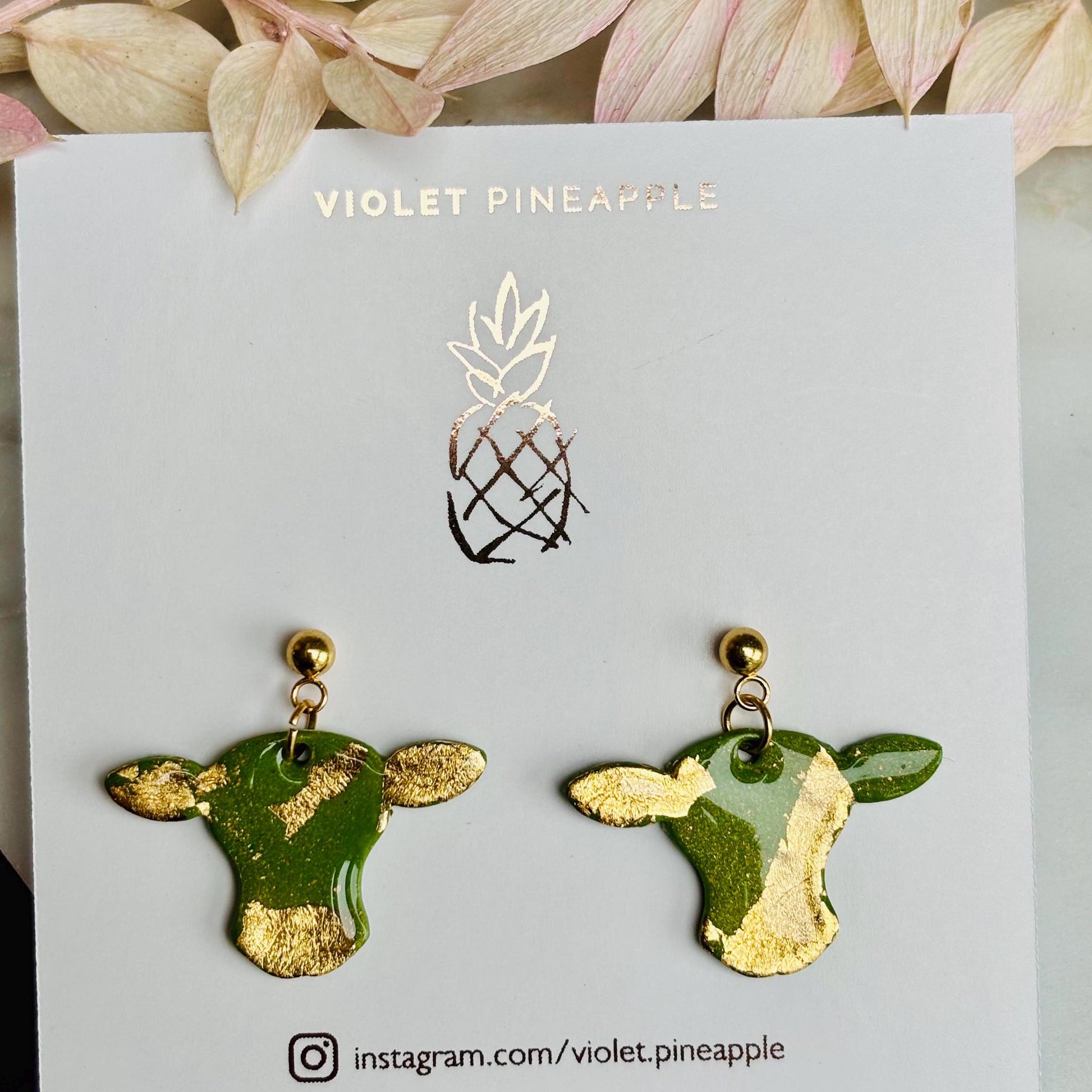 Cute cow drop stud earrings with olive green and gold foil details, handmade with polymer clay.