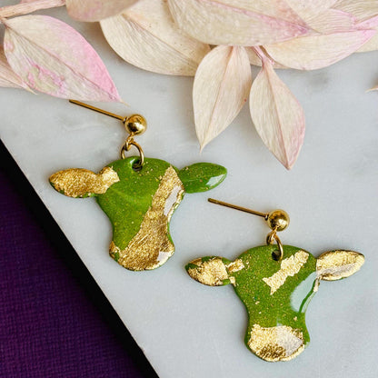 Cute cow drop stud earrings with olive green and gold foil details, handmade with polymer clay.