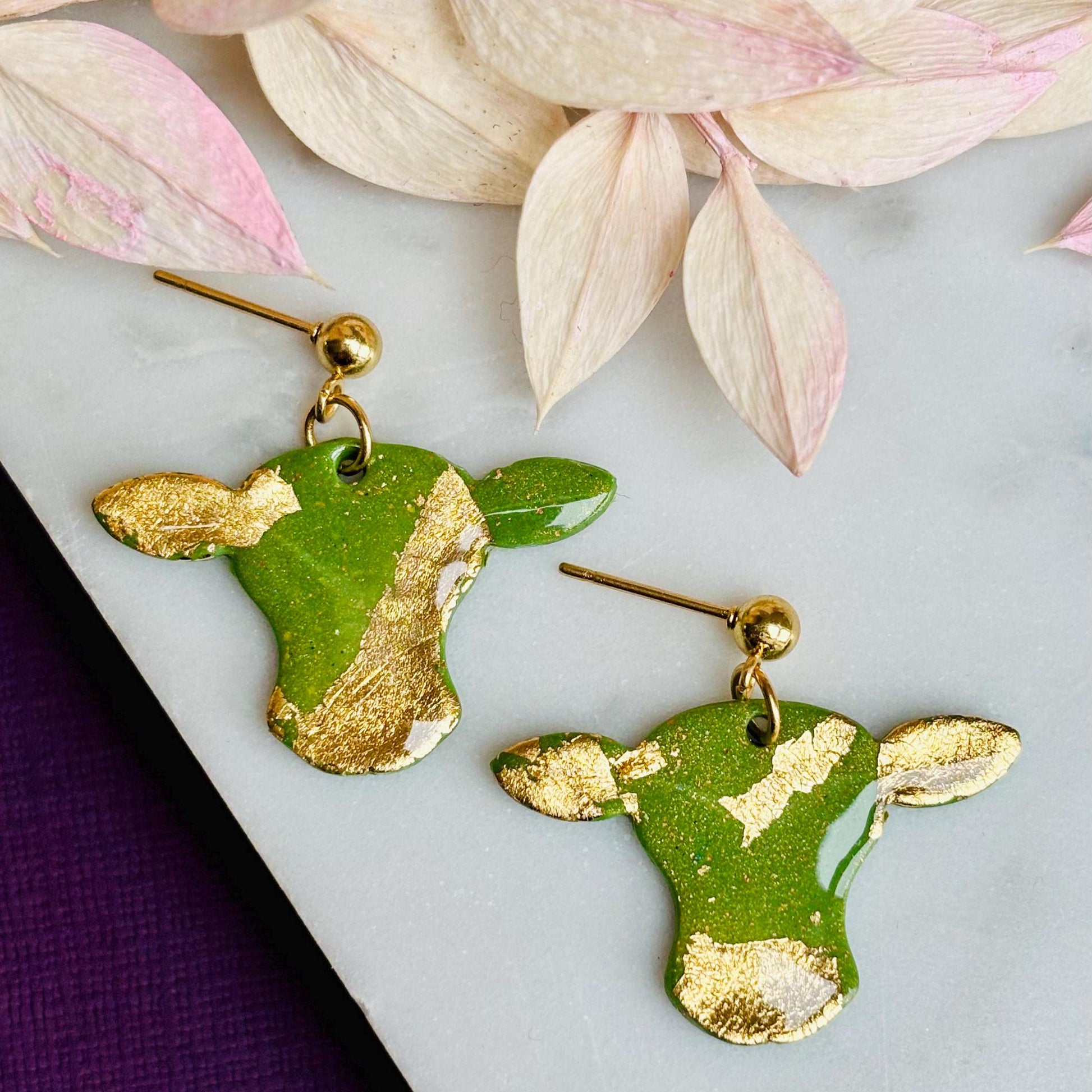 Cute cow drop stud earrings with olive green and gold foil details, handmade with polymer clay.