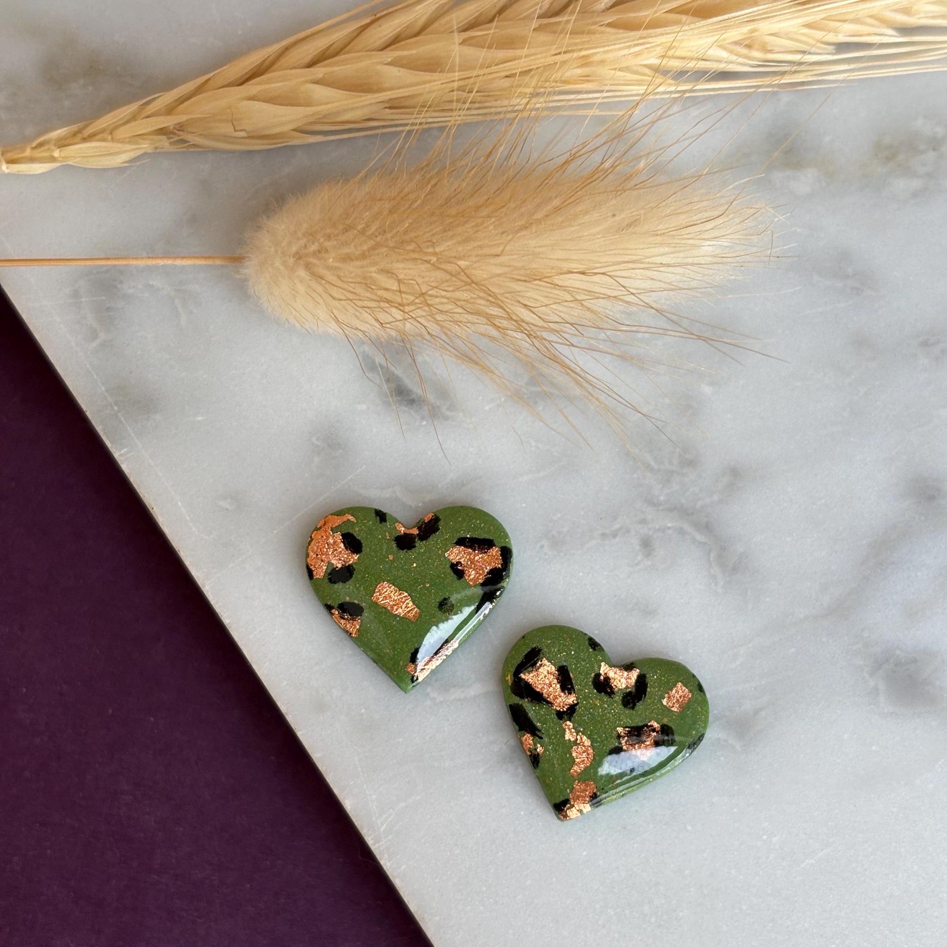 Elegant heart-shaped stud earrings with a hand-painted leopard print, handmade with polymer clay.